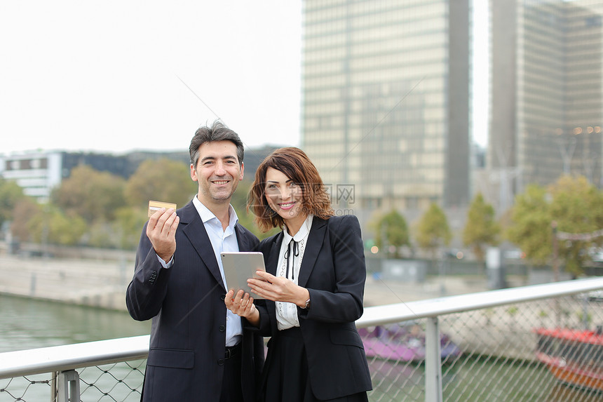 穿着严格的男人和女人通过平板电脑中的信用卡购物车购买商品走在市中心的夫妇妻子突然想起时装店最后几个小时的折扣图片