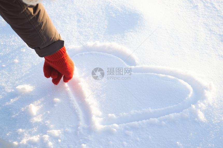 戴红手套的女手在雪地上画心冬天的概念图片