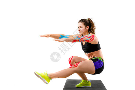 运动员的主题运动学磁带康复美丽的女孩与美丽的战利品做锻炼蹲在白色背景上的黑色地毯上用于治疗肌肉和肌腱的手图片
