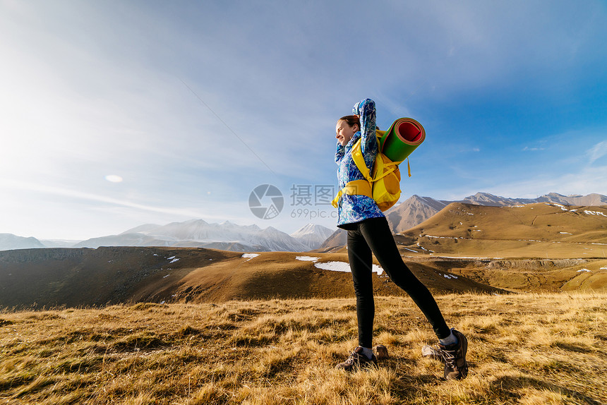 身穿蓝色夹克的活跃年轻女孩带着背包沿着高加索山脊旅行图片
