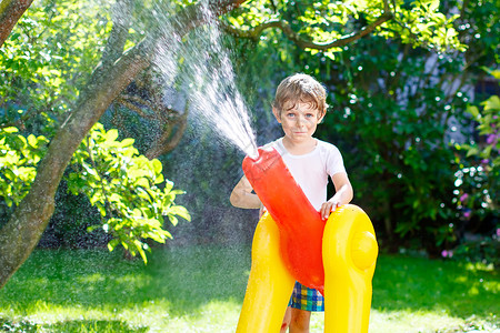 有趣的小男孩在炎热和阳光明媚的夏日玩花园软管洒水器图片
