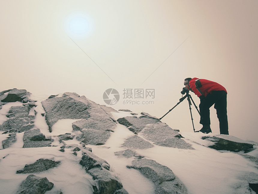 摄影师在三脚架上的相机取景器上停留在白雪皑的悬崖上拍照图片