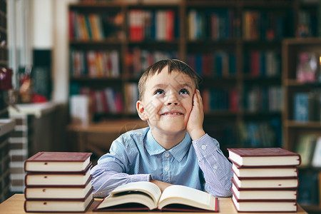 图书馆桌上的单身梦想男孩享受书籍男孩左手放在脸颊上的正面图像欧洲男孩探索书籍学生喜欢讲课教育背景图片