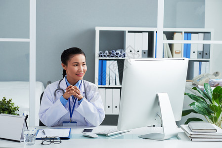 坐在办公室平板和电脑屏幕阅读资料的亚洲女医生图片