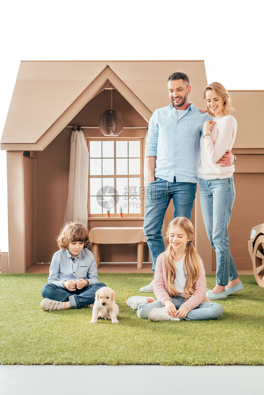 有可爱小狗的年轻家庭在纸板上的房子院图片