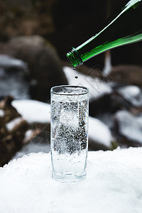 将纯净的矿泉水从绿色玻璃瓶中倒入透明玻璃烧杯中图片