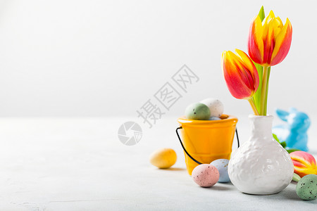 复活节成分包括白花瓶中的春郁金香花和水桶中的有色蛋糖果假日概念图片