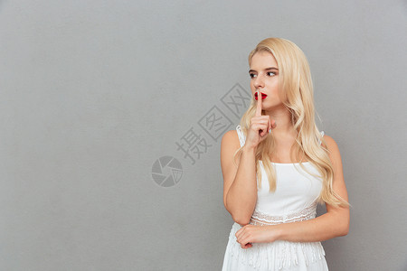 一个年轻女孩的肖像展示沉默的手势望着灰色背景上隔图片