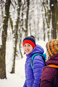 两个微笑的女人在公园里散步背着包的朋友穿过森林在白雪皑的森林背景下图片