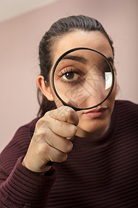 寻找线索或进行调查或搜索的女人透过手持放大镜凝视背景图片