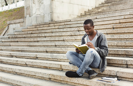 在大学楼梯上微笑的非洲美国学生阅读书图片