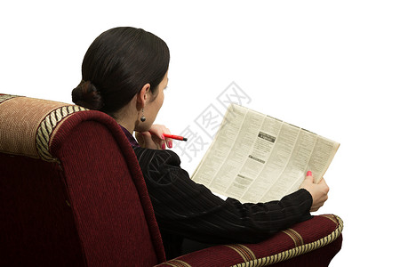 坐在椅子上的年轻妇女为寻找工作而用广告阅读报纸图片