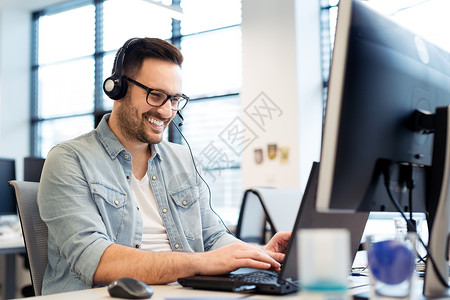 年轻微笑的男呼叫中心接线员用耳机做他的工作办公室呼叫中心工图片
