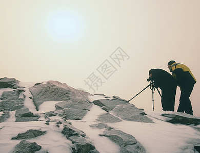 两个男人在雪山中享受冬季摄影自然摄影师用三脚架上的大相机留在白雪皑的图片