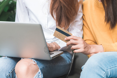 一对年轻的亚洲女在用她的笔记本电脑在线购物时使用她的信用卡的特写年轻女拿着信用卡在花园里网上购物网背景图片