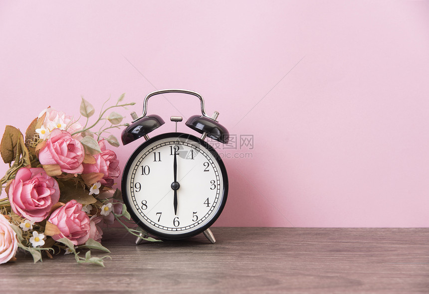 有粉红色背景的木板上的闹钟和玫瑰图片