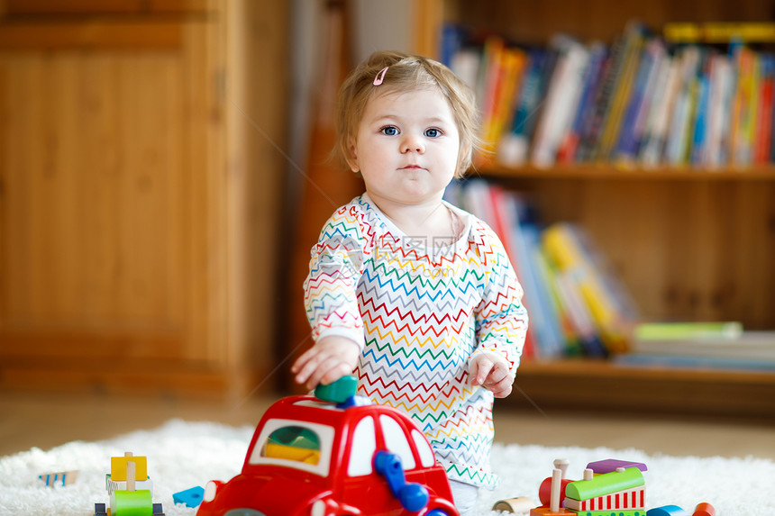 可爱漂亮的小女婴在家里或托儿所玩教育木制玩具蹒跚学步的彩色红汽车快乐健康的孩子玩不同的玩具图片