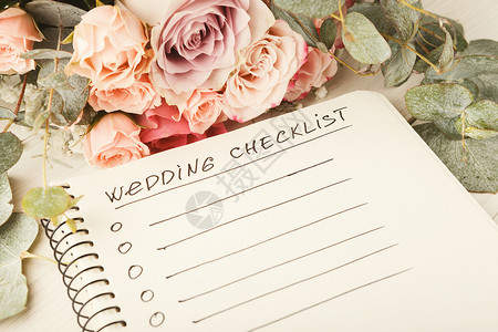 白色桌面上带有复制空间和玫瑰花束的婚礼清单婚姻规划师概图片