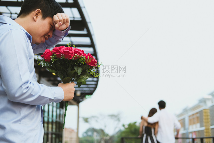 亚洲伤心欲绝的男人拿着一束红玫瑰在看到女人和另一个男人约会时感到悲伤心碎图片