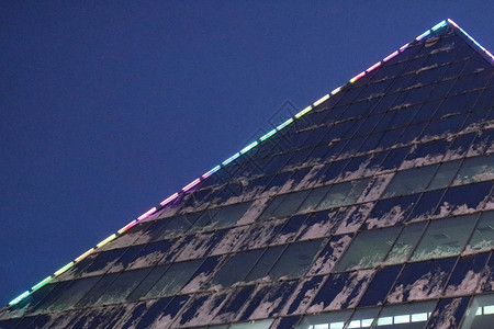 一栋三角形玻璃办公室带发光窗户的现代建筑的一角图片