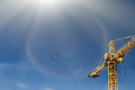 在太阳光束的建筑起重机塔在蓝天背景起重机和建筑工地的工作进展黄图片