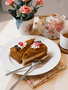 含奶油的蜂蜜蛋糕在白盘上配有叉子茶壶图片