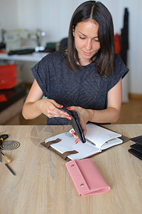 女制作黑色皮革女包女孩喜欢手工艺品和参加缝纫圈戴红指甲的女士坐在桌旁图片