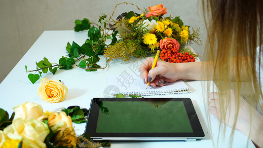 女孩花店在笔记本上用铅笔构思花束和在平板电脑上画草图图片