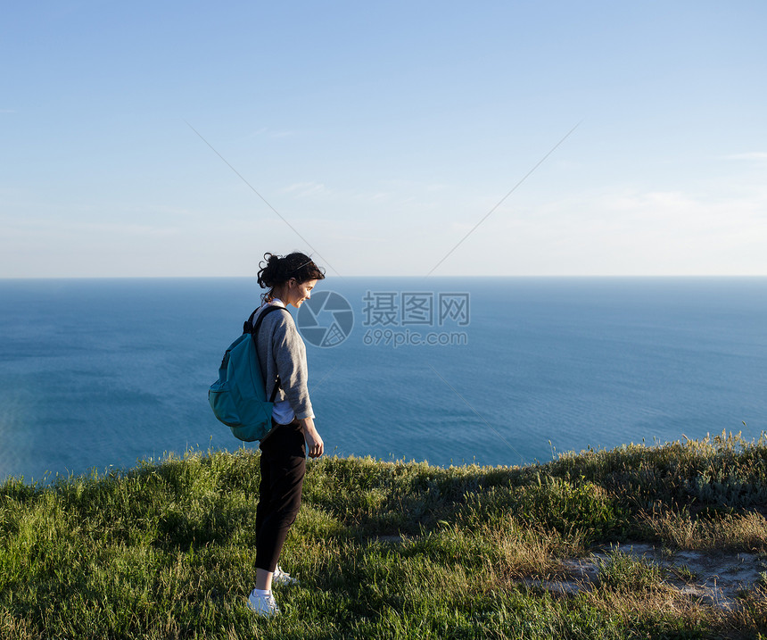 背着包站在山上的年轻女子徒步旅行者微笑的女游客在海边的草地上放松旅行自由和积极的图片