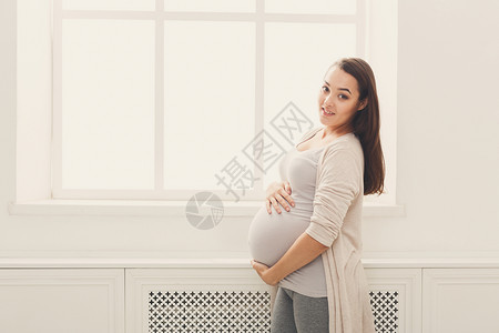 快乐的孕妇在家里爱抚她的肚子图片