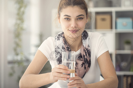 在厨房里拿着一杯水的年轻女人图片