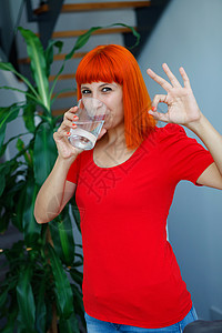 穿着红衣服的红发快乐女人喝着饮用水图片