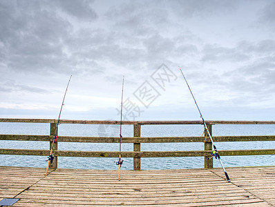 数条钓鱼棒对着海滩码头的木头栏杆图片