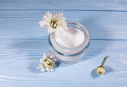 玻璃罐中的化妆品霜白色花朵蓝色木质背景图片