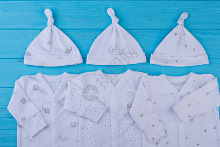 儿童穿带帽子的服装的概念三个婴儿睡衣布与蓝色木桌图片