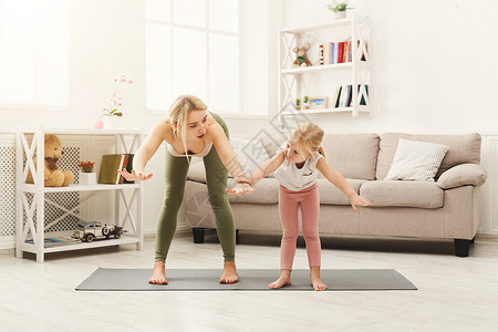 年轻母亲及其小女儿在家里伸展瑜伽锻炼图片