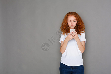 在灰色演播室背景的手机上用手机传递年轻穿刺红头发女青年信息通图片