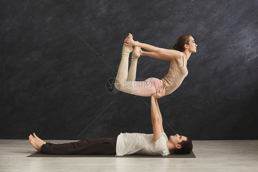 年轻夫妇在健身房的垫子上一起练习Acroyoga女人坐弓姿势复制空间侧观伴侣瑜伽灵活图片