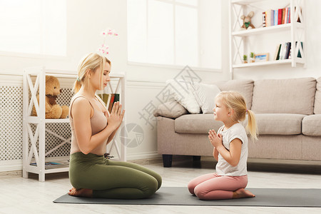年轻的母亲和她的小女儿在家做瑜伽练习活跃的女孩坐在合十姿势准备家庭训练型家庭生活方式背景图片