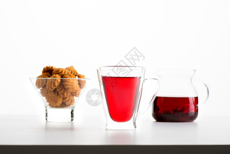桌子上放着装有木槿茶的双层玻璃杯背景上有一个玻璃茶壶和一个图片