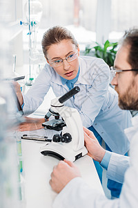 戴眼镜的科学家在工作场所与实验室显微镜一起工作背景图片