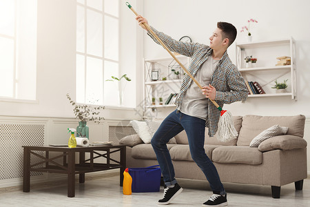 年轻男子或快乐的丈夫在家中打扫玩拖把在客厅里玩得开心图片