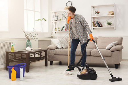 在起居室用拖把和吸尘清洁器打扫家里的年青疲累男子图片