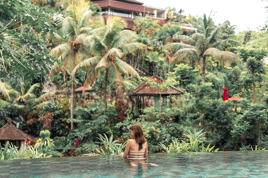 快乐的年轻女子在热带无穷游泳池里巴厘岛豪华度假胜地印度图片