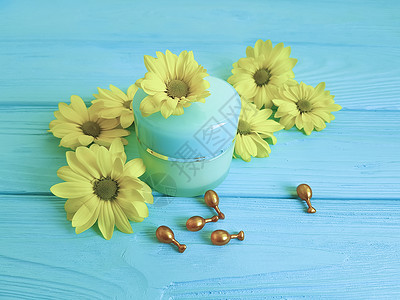 蓝色木质背景上的化妆品奶油黄色花朵甘菊胶囊图片