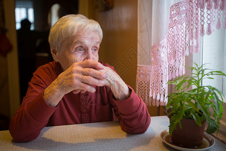 一位老年妇女从坐在桌边的窗户上看图片