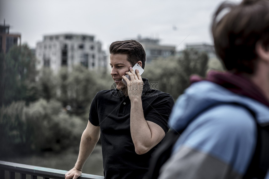 一个男人在手机上说话的中镜头城市建筑和背景中的一条河图片