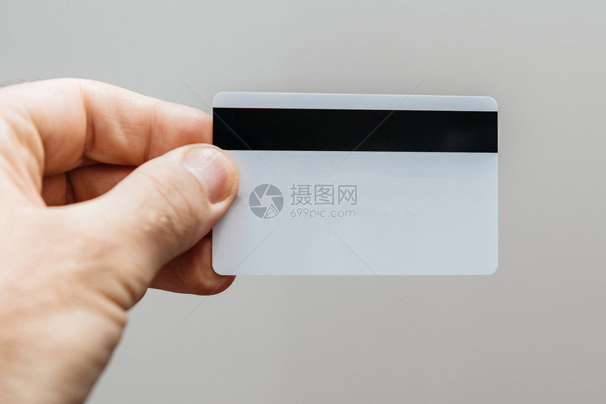 男子在白色背景下持有一张带有磁条和白色内容的信用卡以图片