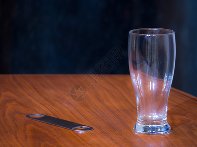 一张黑色胡桃木面板底有深色背景的黑胡桃木颗粒桌子上的空品脱啤酒杯和不锈钢专业开瓶背景图片