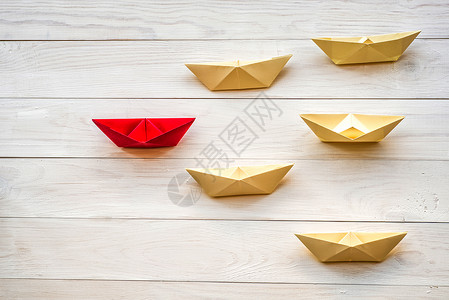 领导理念折纸船跟随白色木制背景的红色船长图片